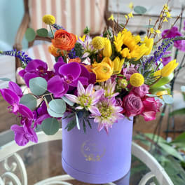 Colorful mixed bouquet in a lavender hat box with orchids, roses, and sunflowers