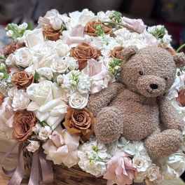 Basket arrangement of white and blush flowers with a teddy bear