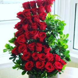 Tall arrangement of red roses with green foliage in a round container