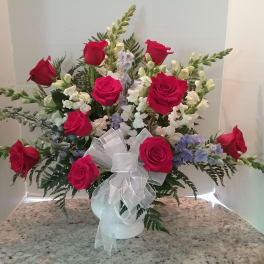 Red rose arrangement in a white vase with a sheer ribbon