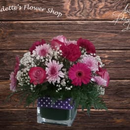 Pink mixed flower arrangement in a square glass vase with a polka-dot ribbon