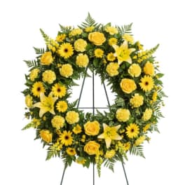 Yellow floral wreath on a stand with lilies, roses, and daisies