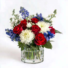 Red roses, white chrysanthemums, and blue flowers in a clear glass vase