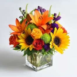 Colorful bouquet with sunflowers, roses, and lilies in a square glass vase