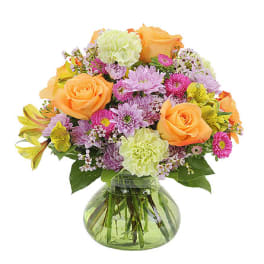 Mixed bouquet of orange roses, pink daisies, and carnations in a glass vase