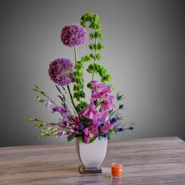 Tall mixed floral arrangement in a white vase with a small orange candle nearby