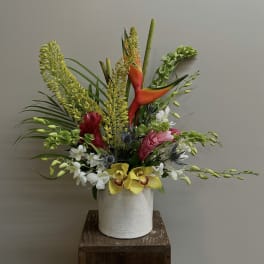 Tropical flower arrangement in a white vase with orchids and heliconia
