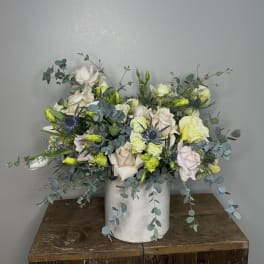 Mixed bouquet of pale roses and blue thistle in a white vase
