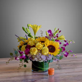 Mixed bouquet with sunflowers, yellow roses, lilies, and purple orchids in a glass vase