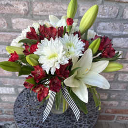 Red and white mixed flower bouquet in a clear glass vase with a striped ribbon bow