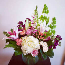 Mixed bouquet of pink lilies, roses, hydrangea, and snapdragons in a round glass vase