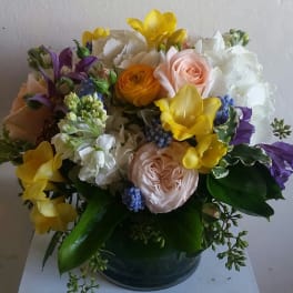 Mixed bouquet of yellow, white, pink, and purple flowers in a dark vase