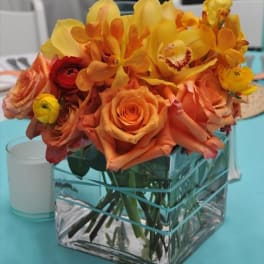 Orange and yellow flowers arranged in a square glass vase