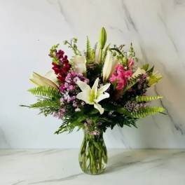 Mixed bouquet of lilies, snapdragons, and pink filler flowers in a glass vase