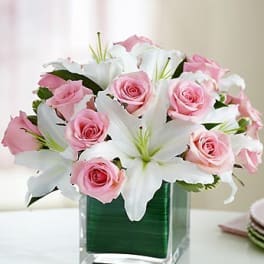 Pink roses and white lilies arranged in a clear square vase