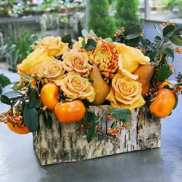 Yellow roses and orange fruit arranged in a rustic wooden box