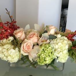 Arrangement of peach roses and white hydrangeas with red orchids in a glass vase