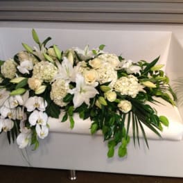 White floral arrangement with lilies, roses, and orchids on a white couch