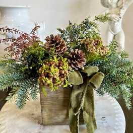 Rustic evergreen arrangement with pinecones and a green ribbon in a wooden box