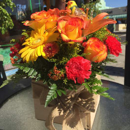 Orange and yellow floral arrangement in a burlap-tied box with a bird decoration