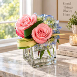 Pink roses and blue hydrangeas in a clear square vase