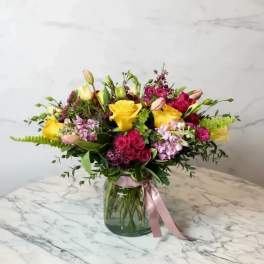 Bouquet of yellow and pink flowers in a glass vase with a pink ribbon