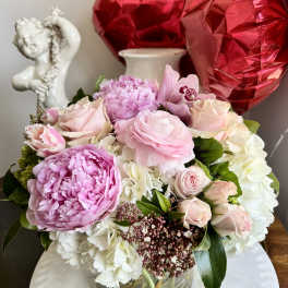 Pink and white flower arrangement in a glass vase with red heart balloons