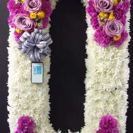 U-shaped floral wreath with purple, white, and yellow blooms and a striped ribbon bow