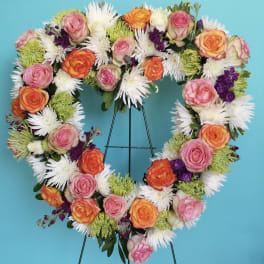 Heart-shaped floral wreath with pink and orange roses on a stand