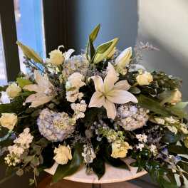 White lilies and pale roses arranged with blue hydrangeas in a low vase