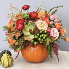 Floral arrangement in a pumpkin vase with orange, pink, and red blooms