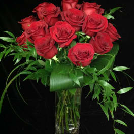 Tall arrangement of long-stemmed red roses with abundant foliage in a clear glass vase