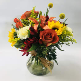 Mixed bouquet of roses, lilies, sunflowers, and carnations in a glass vase