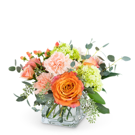 Orange and pink roses with pale green hydrangeas in a clear glass vase
