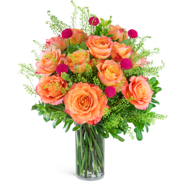 Orange roses in a clear glass vase with pink accent blooms
