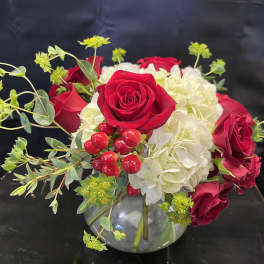 Red roses and white hydrangeas in a glass vase with red berries