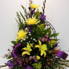 Tall floral arrangement with yellow lilies and purple flowers in a black basket