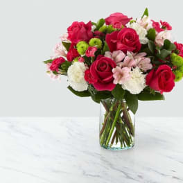 Bouquet of pink roses, white flowers, and green pompons in a glass vase