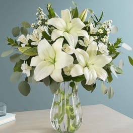 White lilies and small white daisies in a clear glass vase