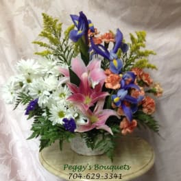 Mixed bouquet with pink lilies, blue irises, and white daisies in a basket