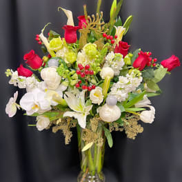 Red and white floral arrangement in a clear glass vase with gold holiday accents