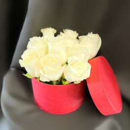 White roses in a red round box with the lid beside it