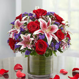 Red roses and pink lilies in a glass vase with purple filler flowers