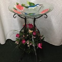 Glass birdbath with pink flowers and a floral base arrangement