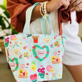 Small aqua tote bag with colorful cartoon floral and character print held by a person.