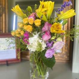 Bouquet of yellow lilies, roses, and purple flowers in a clear glass vase