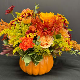 Autumn floral arrangement in a pumpkin-shaped container with orange and yellow blooms