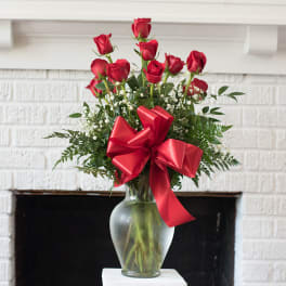 Red roses arranged in a clear glass vase with a large red bow