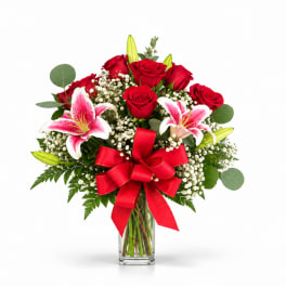 Red roses and pink lilies in a clear glass vase with a red bow