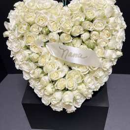 Heart-shaped arrangement of white roses with a satin ribbon on a black box